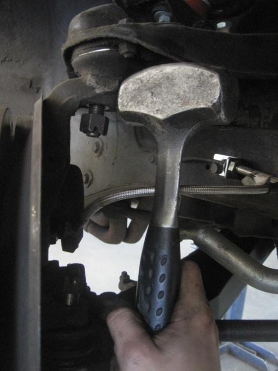 17) Take a hammer and hit the spindle to loosen the upper control arm ball joint. a. Remember to keep the castle nut on the ball joint to protect the threads.