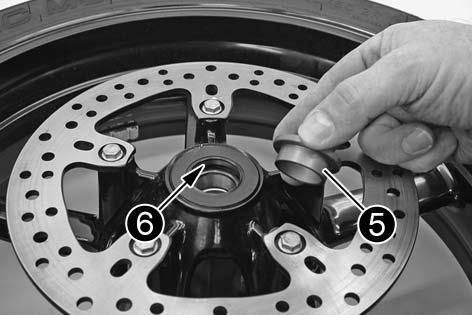 Allow the brake caliper support and swing arm [A] dollies to engage, place the chain on the gear wheel and mount the wheel spindle.