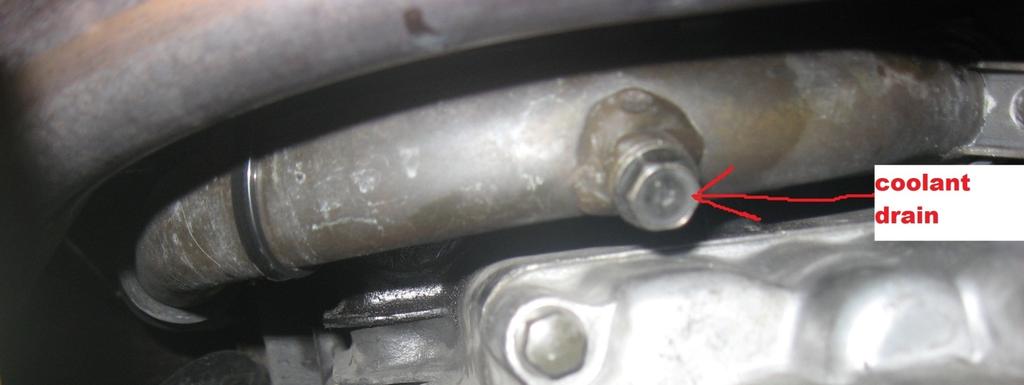 Figure 7: The coolant drain bolt is on the bottom of the metal line shown. This photo was shot on the floor of the garage, looking up on the bottom of the engine.