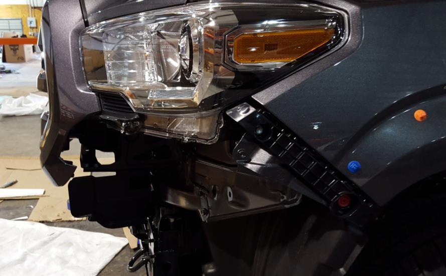 L. Using a 10mm socket and a flathead screwdriver, remove the bolt and pop pin holding on the plastic under the headlights. Remove the plastic piece and replace the bolt to secure the headlight.