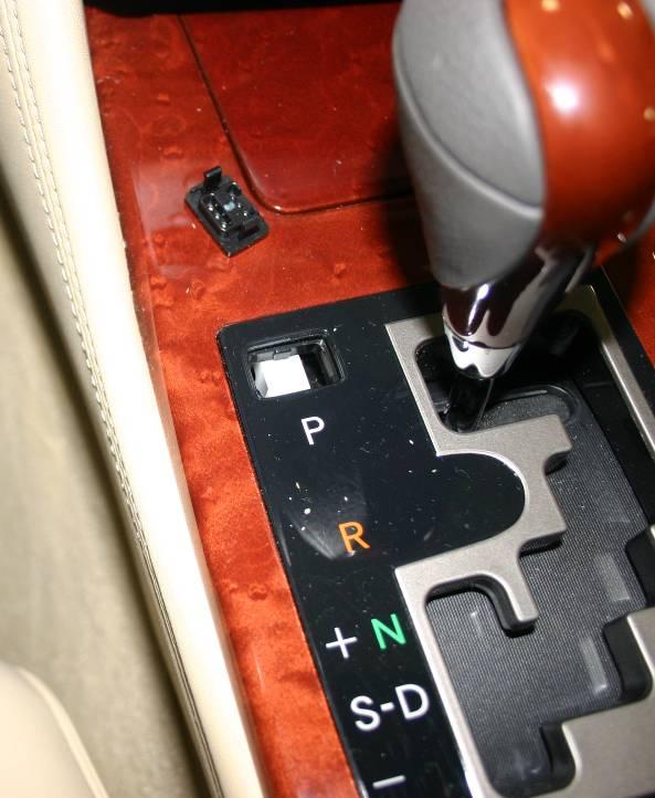 This is accomplished by lifting out the small cover above the shifter Park (P) indicator and depressing