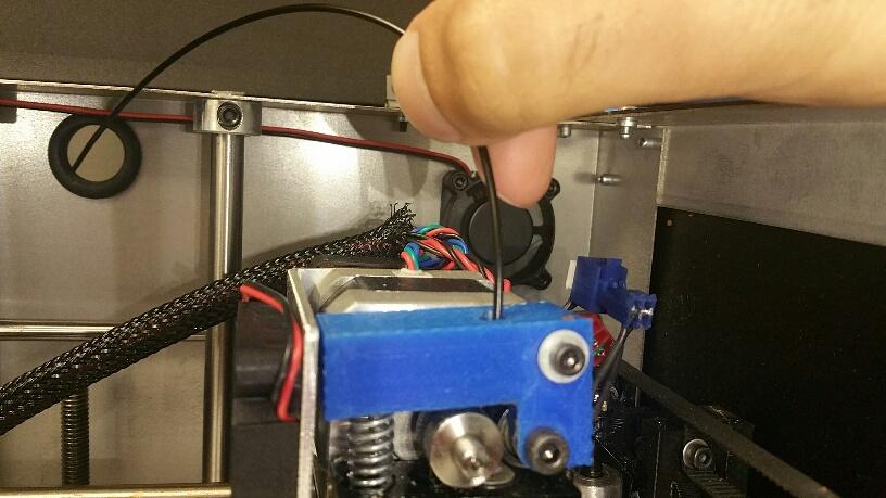 19. Inside the 3D printer, pull the plastic through the hole further until it reaches the nozzle. Push the plastic through the top of the nozzle assembly until it touches the two disks.