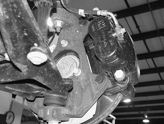 Remove the two brake caliper mount bolts and remove the caliper assembly from the knuckle Figure 3. Hang the caliper securely out of the way.