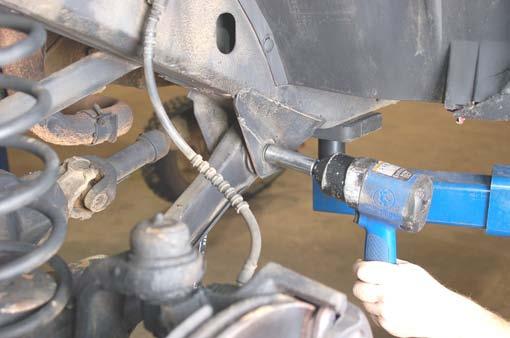 Locate and remove the coil clip on the driver side lower coil spring seat using a 13mm wrench. Lower the axle to allow for removal of the coil spring. Do not overextend the brake lines.
