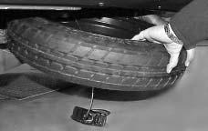 When the spare tire has been completely lowered, tilt the retainer and slip it through the wheel opening. 10.