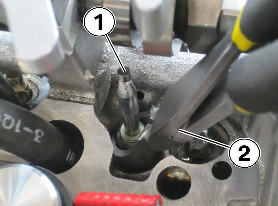 31. Install the new valve seal (1) with the angled seal pliers included in the tool kit (2). Push firmly to seat the valve seal. Repeat this process on the adjacent valve. 32.