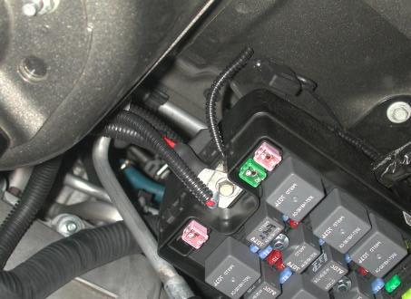 15. The harness with the inline fuse is to be routed across the front of the vehicle to the 12V+ bolt on the edge of the fuse box located on the passenger s side. See Photo 6 below of 12V+ location.