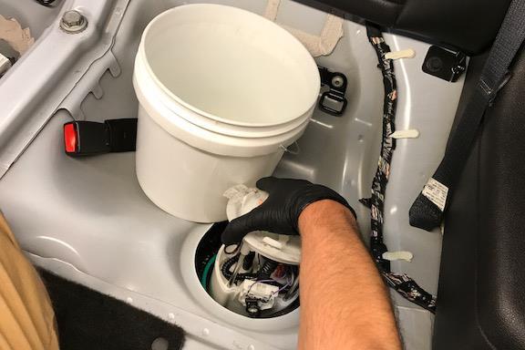 Squeeze the thumb tab and pull away to release the crossover hose, as shown. Pull the OEM fuel pump housing out and drain into the bucket. Inspect the large green gasket.