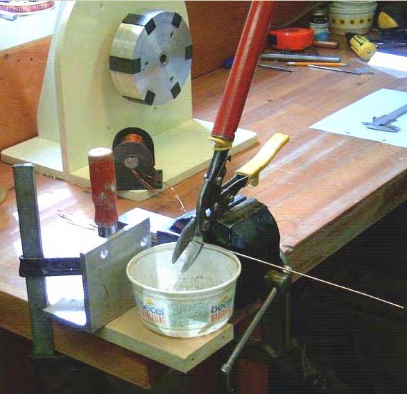 THE DISTANCE BETWEEN THE SHEARS AND THE METAL CLAMPED TO THE WORKBENCH MAKES EACH CUT LENGTH OF WIRE EXACTLY THE SIZE REQUIRED, WHILE THE PLASTIC CONTAINER COLLECTS THE CUT PIECES READY FOR COATING