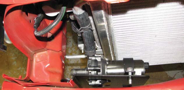 Route the long molded hose under the fuse box to the intake of the water pump.