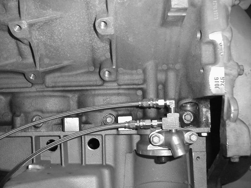 Install the pipe and clamps that was previously laid bay like shown below but do not tighten yet. Remove the oil transfer cover located above the oil filter that holds the temperature sensor.