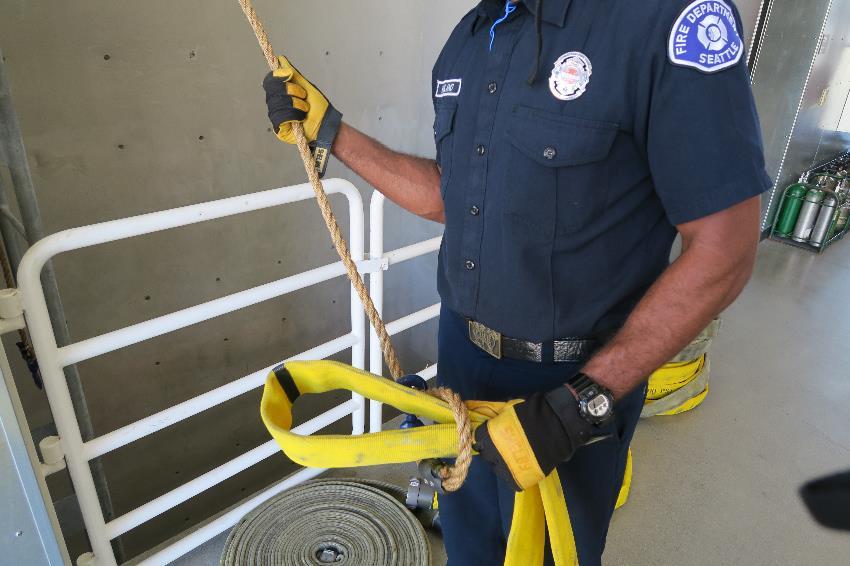 While holding the bend in the hose at the halfway mark, the firefighter takes a turn with the halyard and hooks the rope.