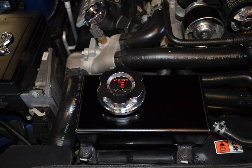 9. Grab the C&R Coolant Engine Coolant Reservoir and attach the larger coolant line to the bottom of the tank a) Use pliers to loosen the hose clamp and slide it over the line to clamp it in place.