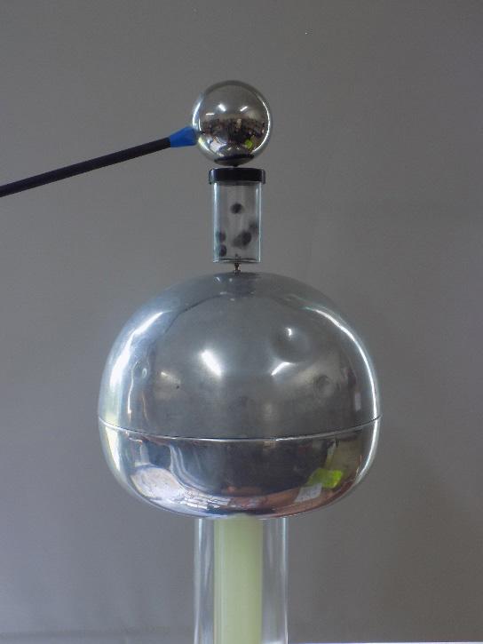 (d) A smaller Van de Graaff generator is used for a class activity. The teacher places a container of conductive balls onto the top of the Van de Graaff generator, as shown in the picture.