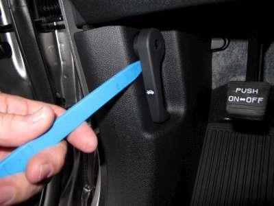 9. Using a NRT, pry off the hood release handle. Pull up and remove lower panel.