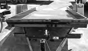 To lower the trailer bed to the ground, unlatch the bed by depressing the bracket and lifting the lever.