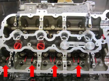 Install the U-bend plug brush (1) into the cylinder head drain back hole just below the exhaust camshaft (see arrow).