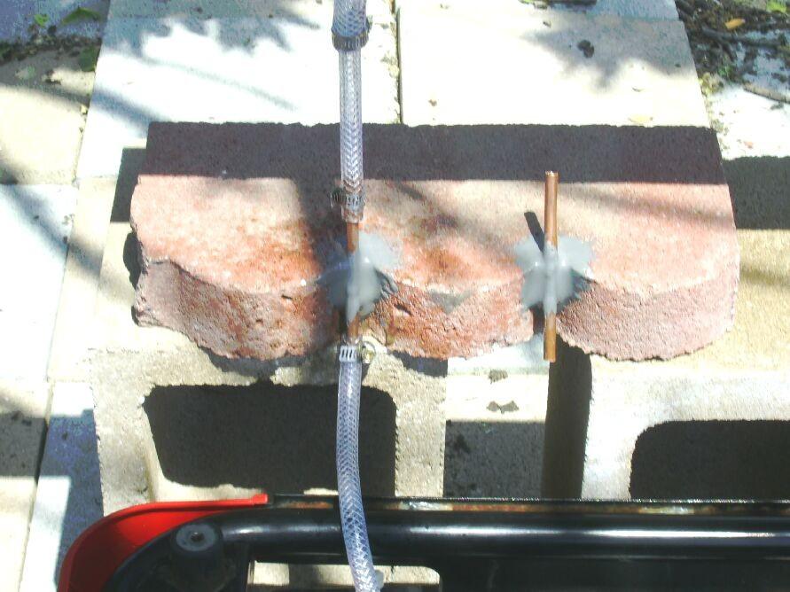 This photo shows how a piece of copper tubing is glued, with JB Weld, to a piece of concrete. The concrete piece is sitting on two concrete blocks.