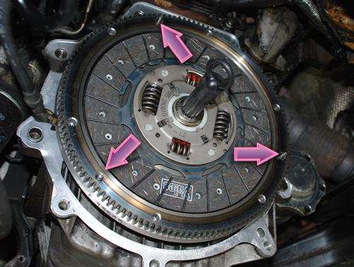 Cross-tighten and torque the new bolts to 10 ft-lb initially to ensure that the flywheel is seated uniformly. Install a flywheel lock (arrow).