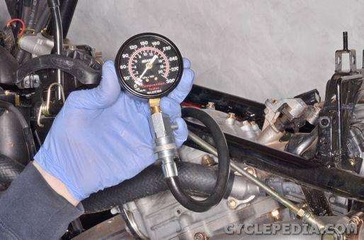 Install the compression tester into the sparkplug hole using a compression gauge adapter and tighten it hand tight. Hold the throttle wide open and use the electric starter to turn the engine over.