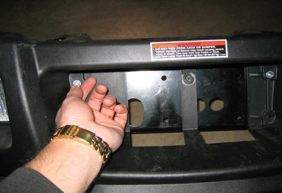 From behind the bumper, use a 3/8 socket or wrench to remove the two screws holding the bumper center panel cover.