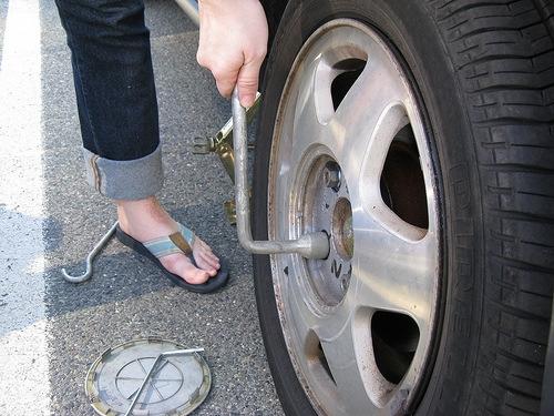 Then one must locate the lug wrench (sometimes the wrench is the handle of the jack) and loosen the lug nuts on the tire. One can optionally do this prior to lifting the car with the jack.