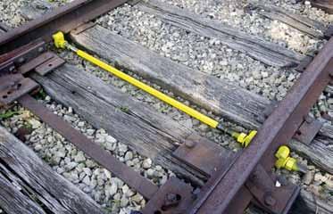 A pair of iron jaws at each end of the double-ended gauge rod grip the rail base to hold the rails to gauge and keep the rails upright against wheel pressure.