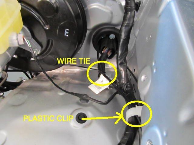 through the plastic clip 4. Locate the large vehicle harness grommet on the left side.