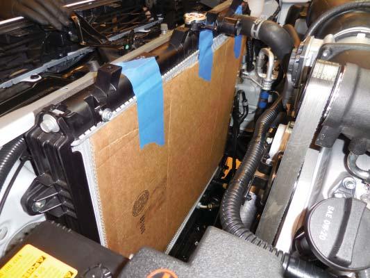 281. Remove the cardboard from the back of the radiator and replace the fan shroud, fan, radiator reservoir, and hoses following