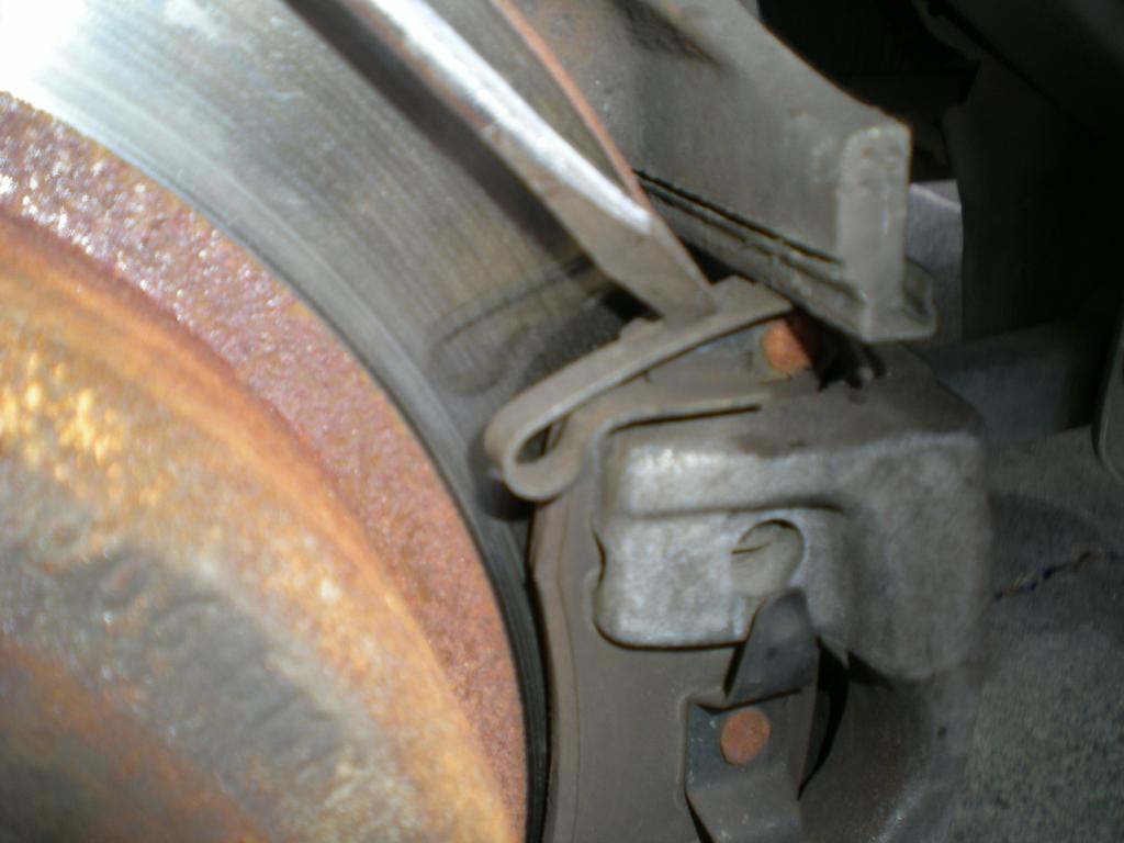 Press down on this retainer spring to allow the caliper to