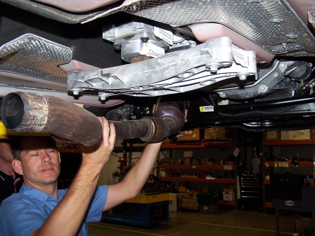 Pull the stock catalytic converter down and off the cast manifold studs while twisting the